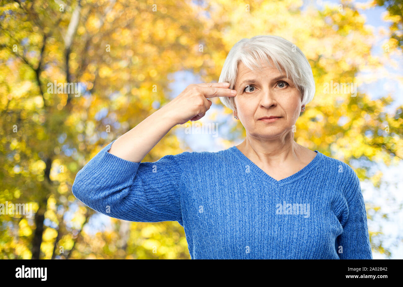 old woman making finger gun gesture in autumn park Stock Photo