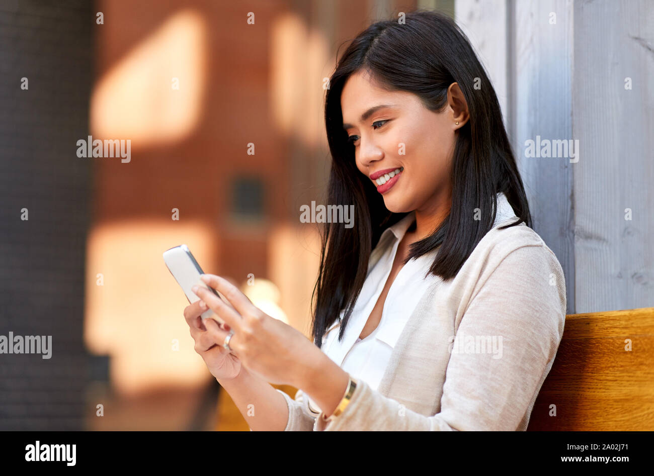 asian woman using smartphone sitting on bench Stock Photo