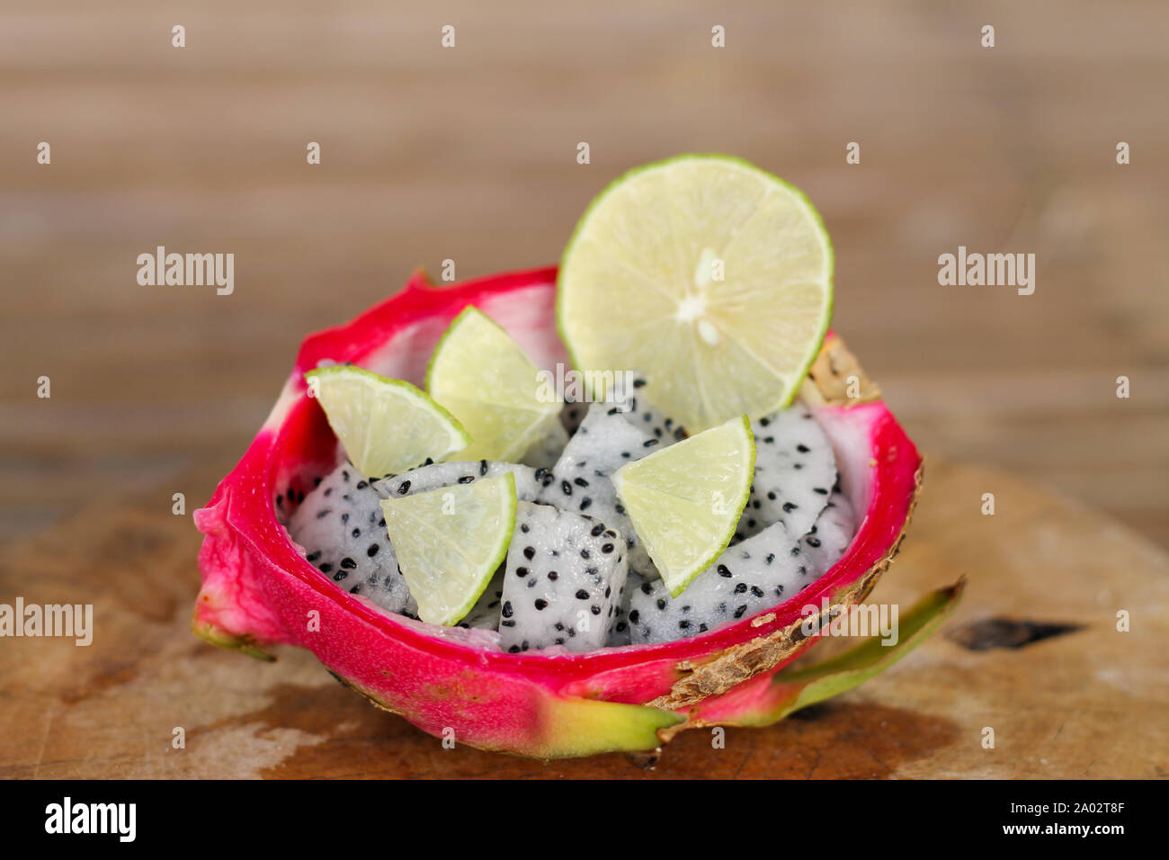 Dragon fruit sliced and lime slice in a haft of dragon fruit peel on old wooden table background. Stock Photo