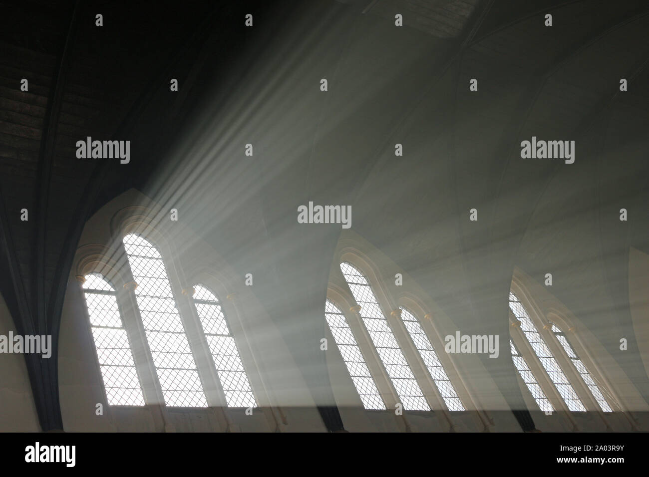 Sunlight streaming through the windows of a church highlighted by the smoke from burning incense and candles. Stock Photo