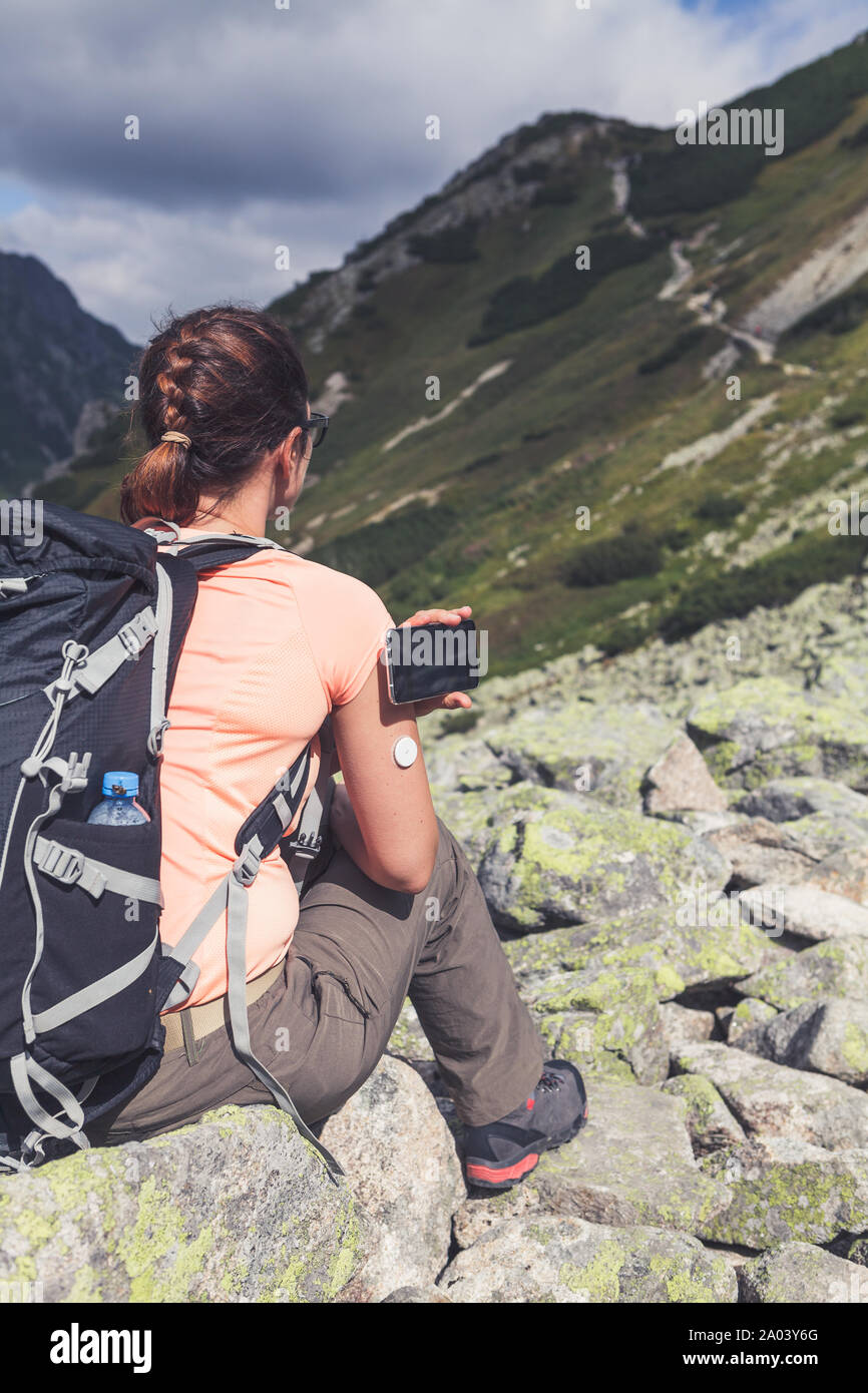 Active life of diabetics, woman hiking and checking glucose level with a remote new technology sensor and mobile phone without blood Stock Photo
