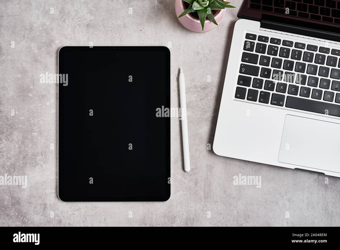 Open laptop with digital tablet and white pencil on grey concrete background. Top view with copy space for text. Flat lay. Stock Photo