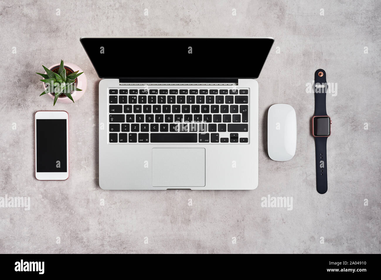 Open laptop with white mouse, smartphone, smartwatch and plant on grey concrete background. Top view with copy space for text. Flat lay photo of offic Stock Photo