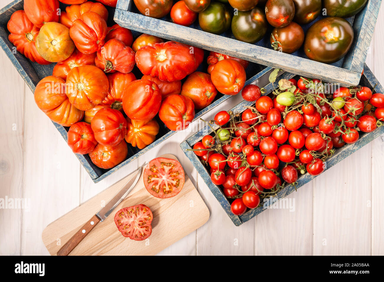 Variety Fresh tomatoes in crates on wooden background. Raf, cherry and kumato tomatoes. Stock Photo