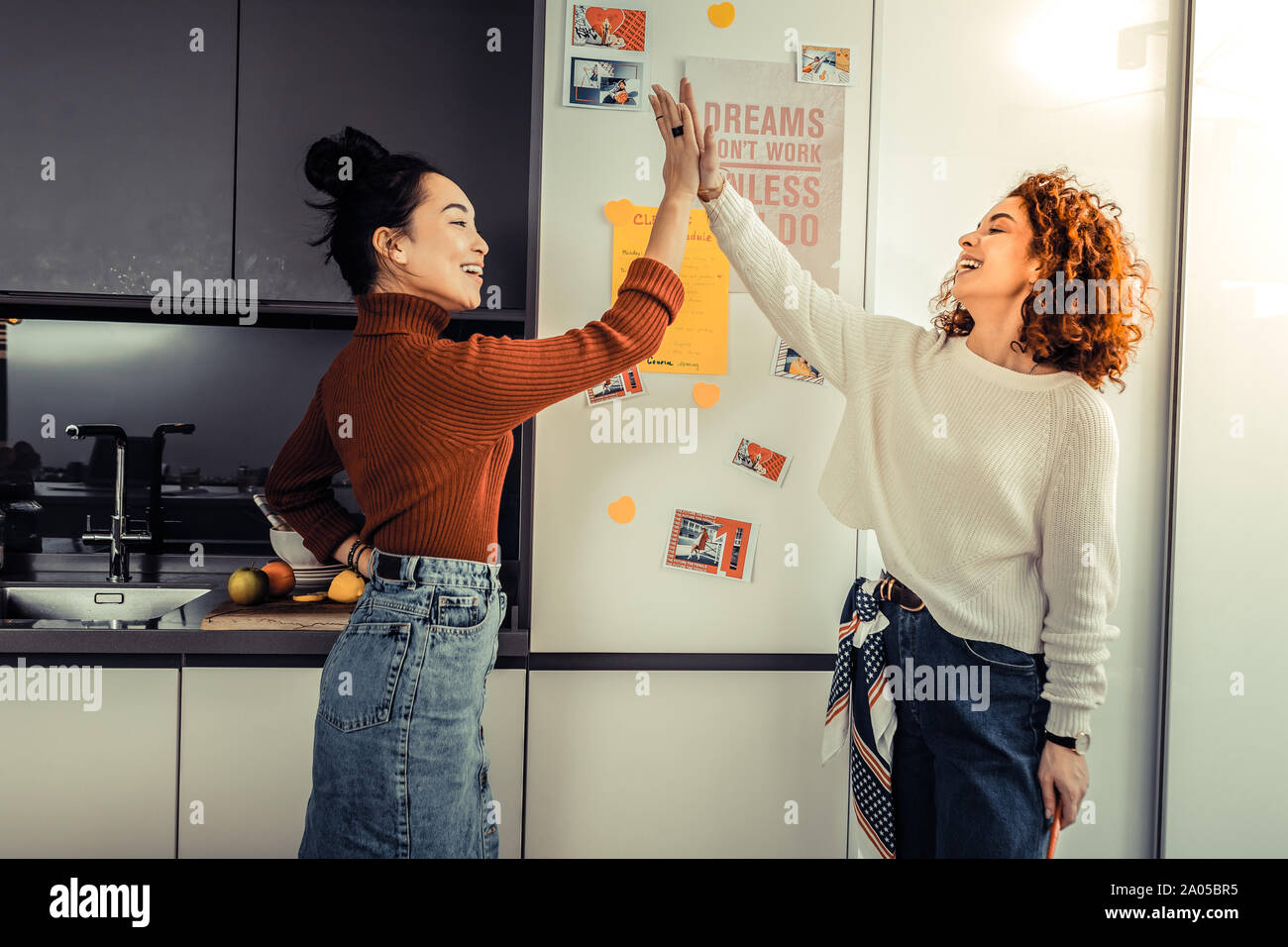 Two cheerful young women giving a high five to each other standing in ...