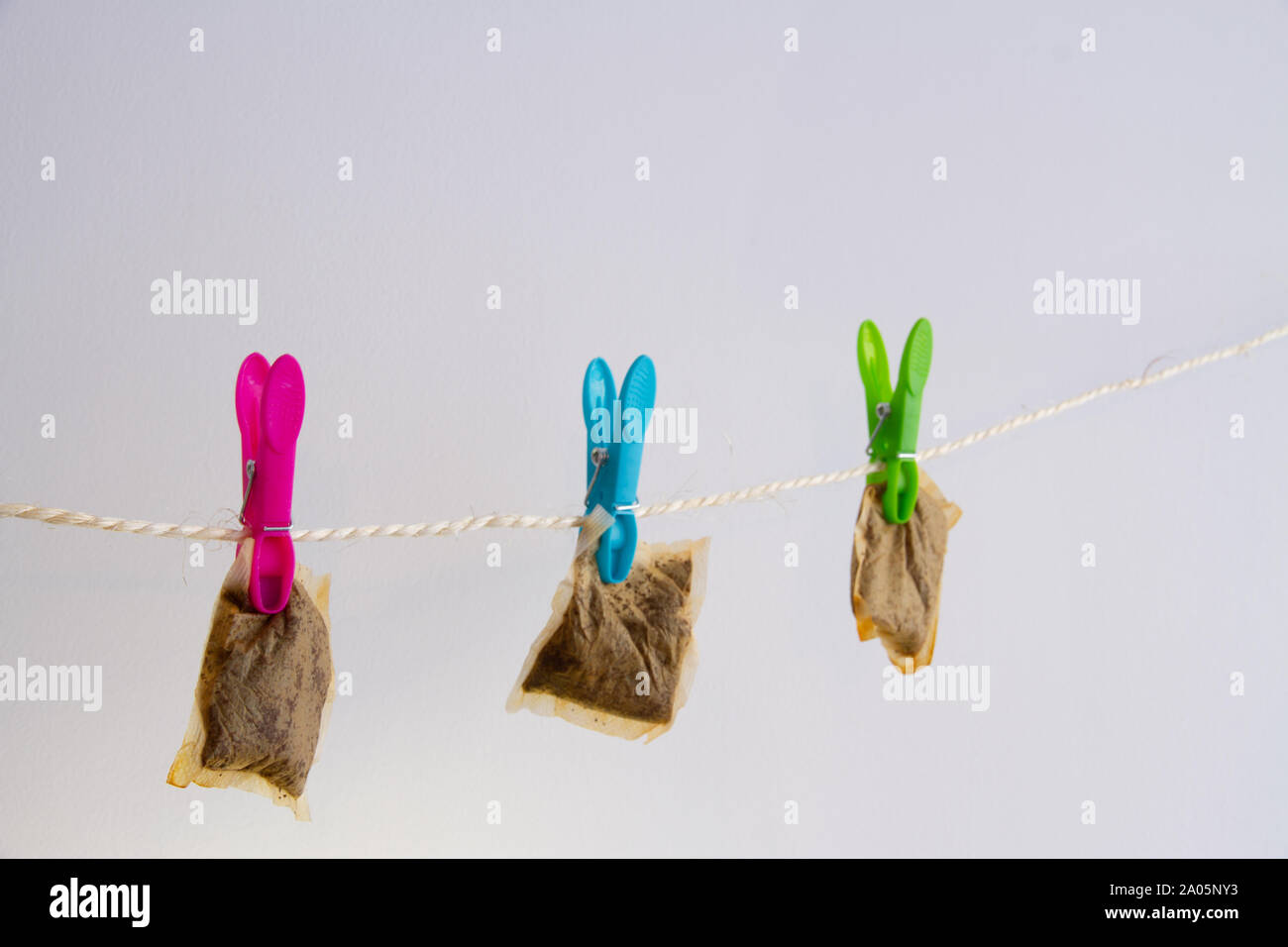 Three used teabags hang to dry on a washing line with colourful pegs, against a neutral background, representing frugality Stock Photo