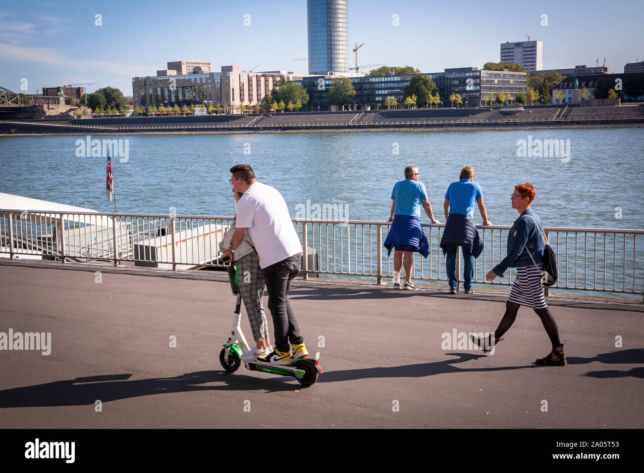 couple on a electric scooter of the company Lime on the banks of the river Rhine, Cologne, Germany. Church Gross St. Martin and the cathedral.  Paar a Stock Photo