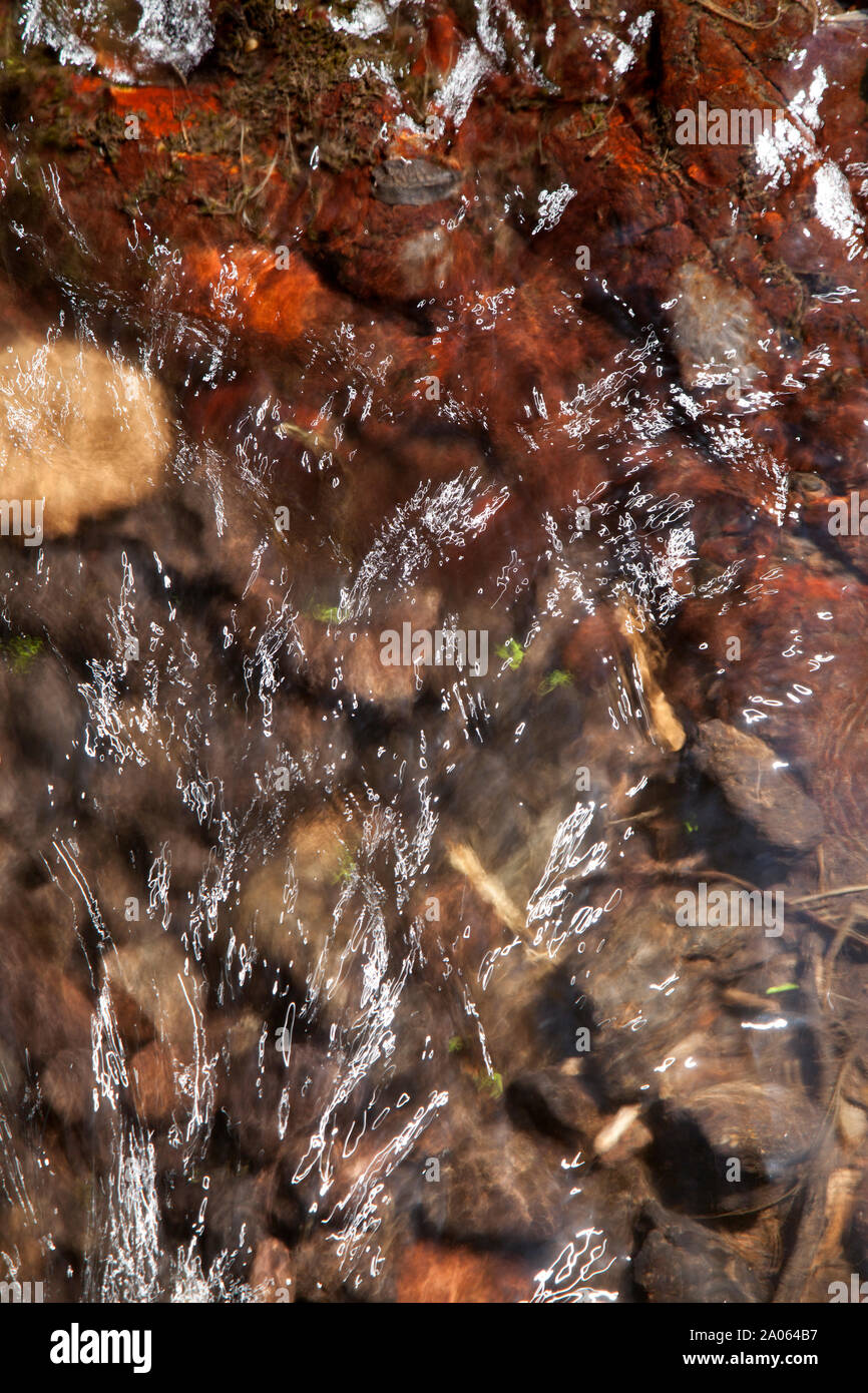 running water abstract, red, iron-rich rocks under shining water Stock Photo