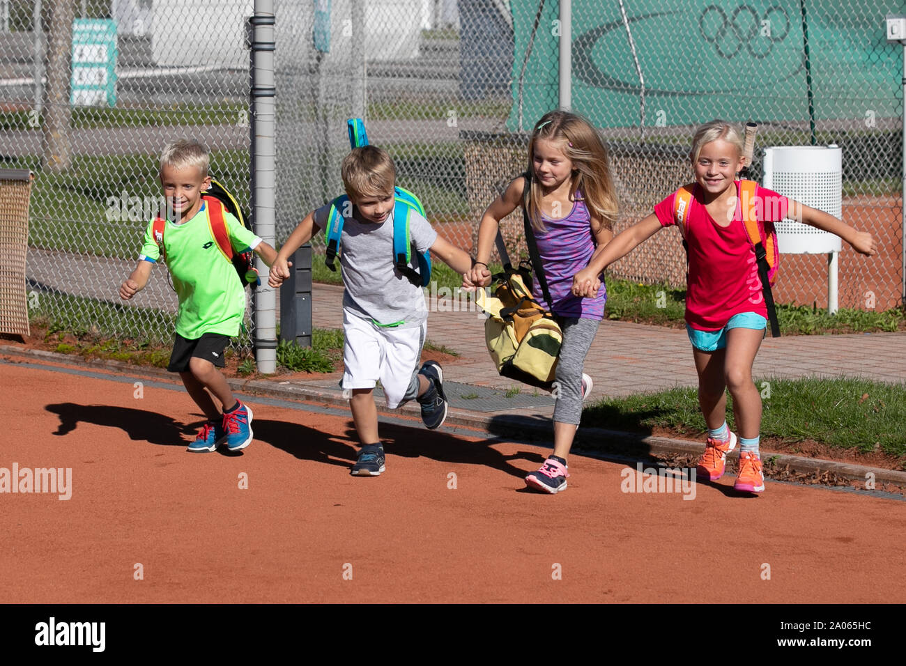 Children with bags and rackets running onto tennis court Stock Photo