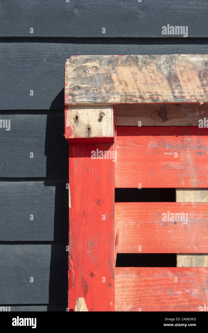 Orange pallett leaning against a black wooden shed Stock Photo