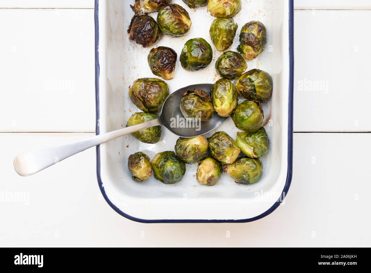 Brassica oleracea. Roasted Brussel sprouts in a white enamel roasting dish with spoon on a white wooden  background Stock Photo