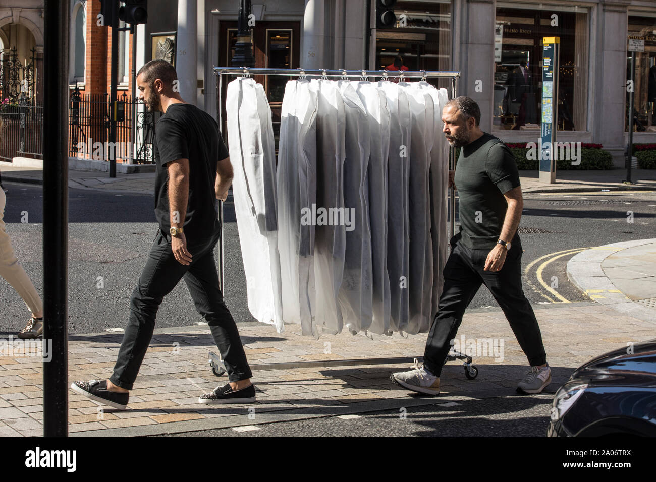 Fashion assistants transport to a boutique a clothes rail down South Audley Street in Mayfair, London, England, UK Stock Photo