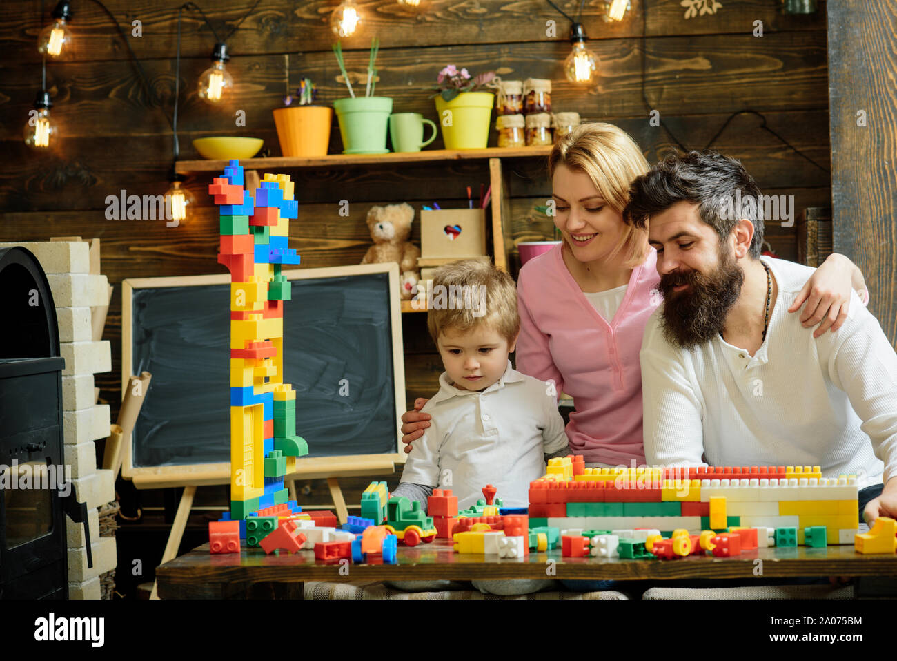 Concentrated boy building wall of colorful plastic blocks. Smiling mom ...
