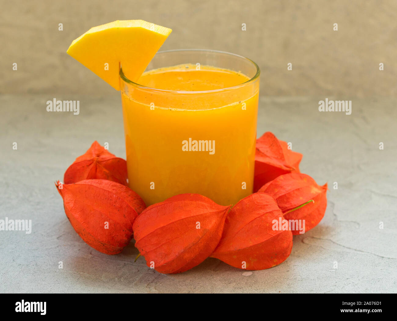 A glass of fresh pumpkin juice and pumpkin on a table decorated with physalis flowers. A concept of healthy seasonal smoothies and juices. Stock Photo