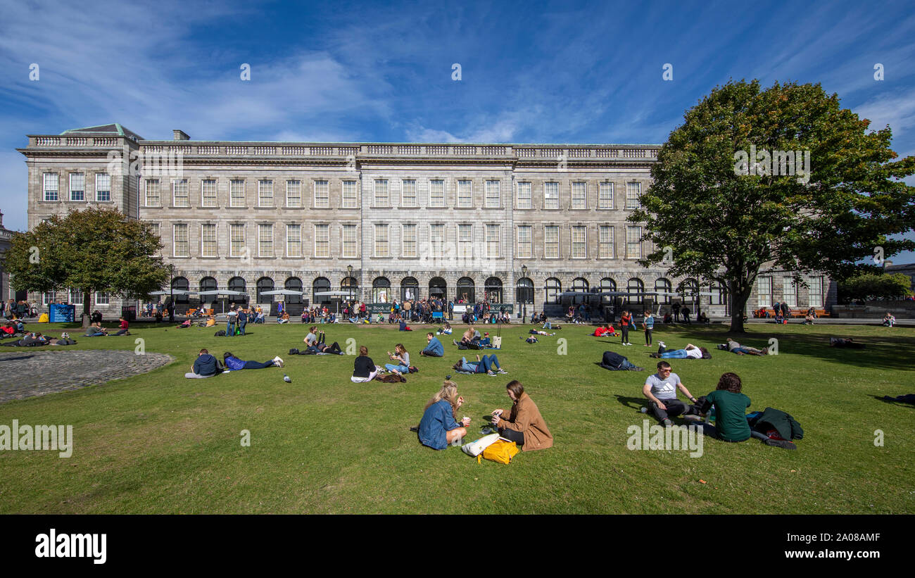 Students relaxing and ejoying a leisurely day with beautiful weather on the lawn outside The Book of Kells, Trinity Old Library in Dublin, Ireland. Stock Photo