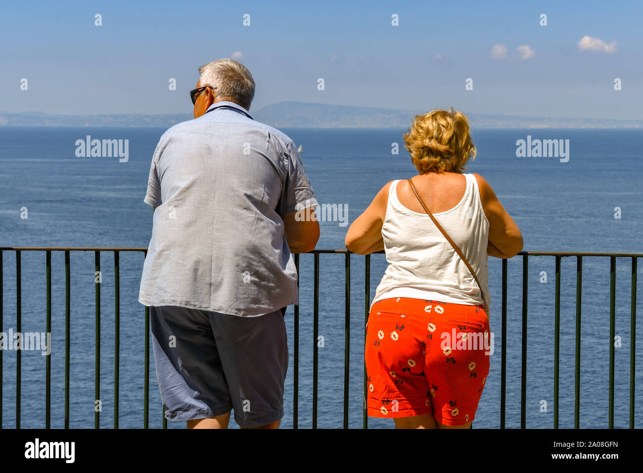 SORRENTO, ITALY - AUGUST 2019: Man and woman leaning on metal railings on the clifftop in Sorrento looking out to sea Stock Photo