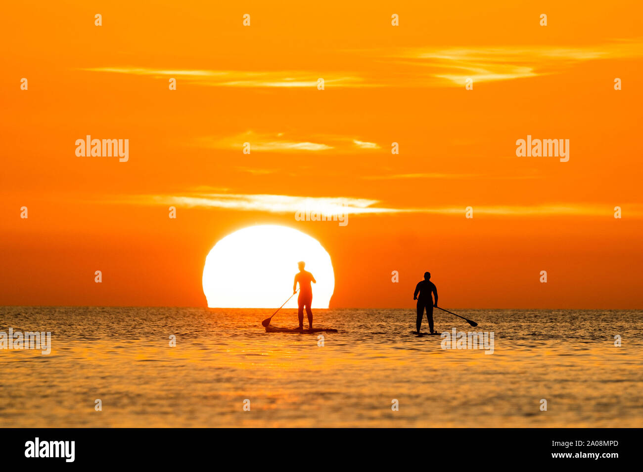 Aberystwyth Wales UK, Thursday 19 September 2019  The sun setting gloriously over  Cardigan Bay silhouettes people on their paddle-boards on the sea at the end of a day of unbroken clear blue skies and warm September sunshine in Aberystwyth, west Wales.   as the ‘indian summer’ mini heat-wave continues over much of the souther parts of the UK  Photo credit Keith Morris / Alamy Live News Stock Photo