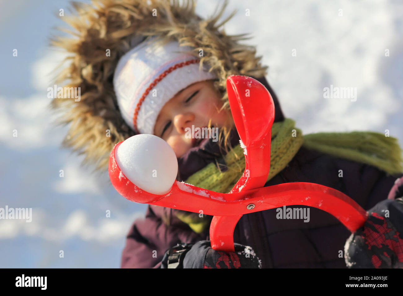 Three year old girl playing with a red snowball maker outdoors Stock Photo