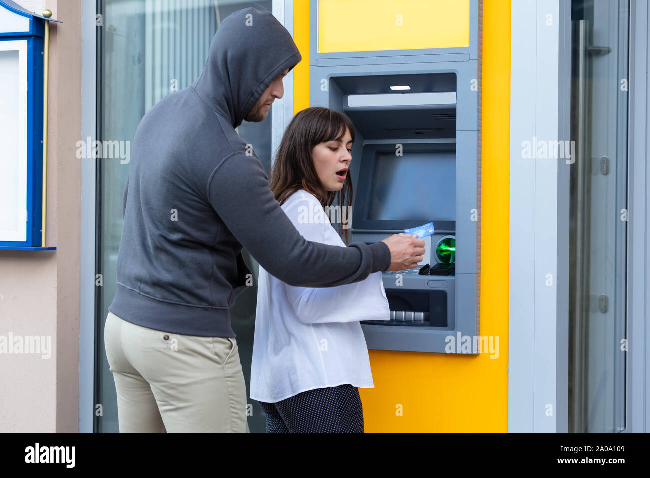 Aggressive Thief In Gray Hoodie Stealing Card From Woman Standing Near The Automatic Teller Machine Stock Photo