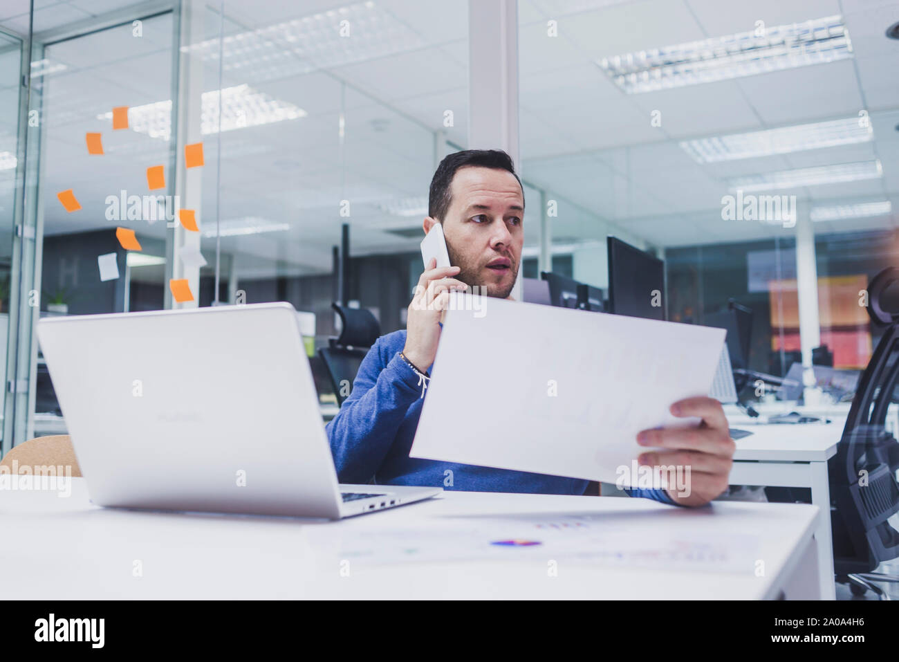 Male executive talking on mobile phone while using laptop at desk Stock Photo