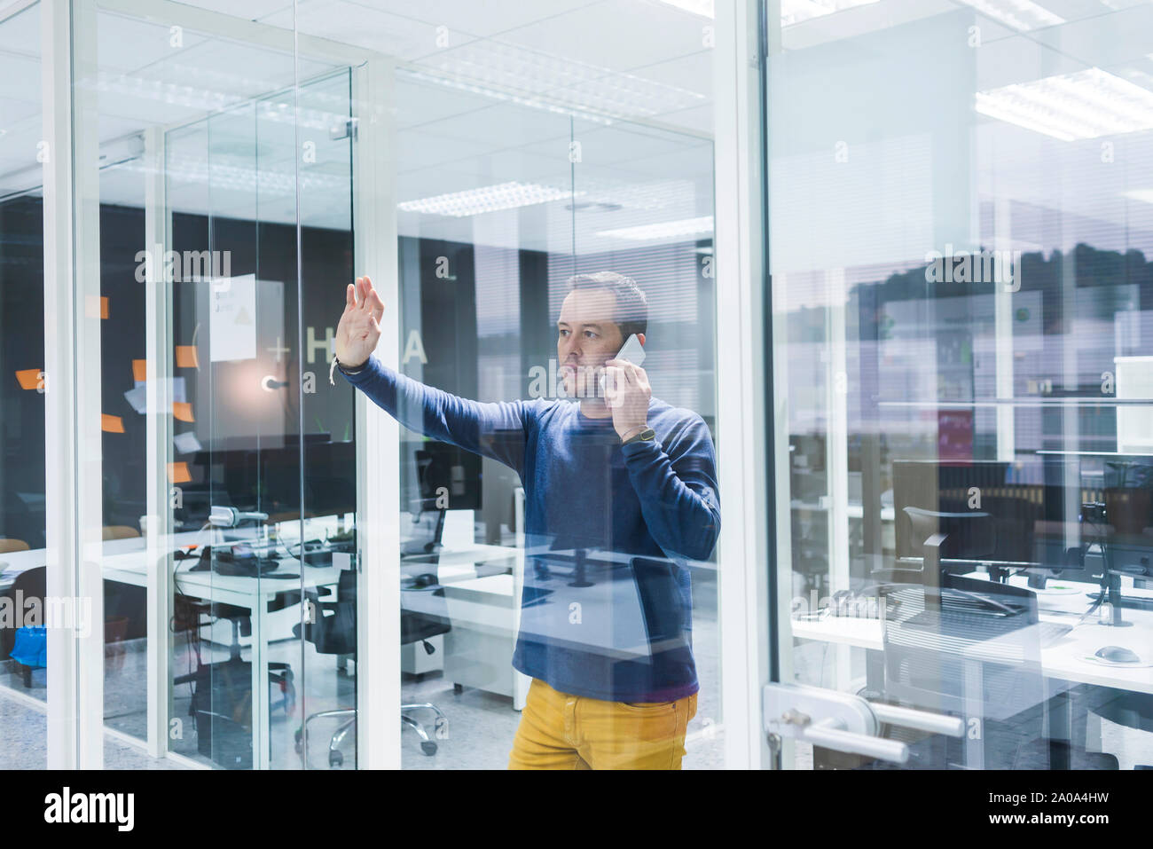 Side view of businessman talking on smart phone while standing against office wall Stock Photo