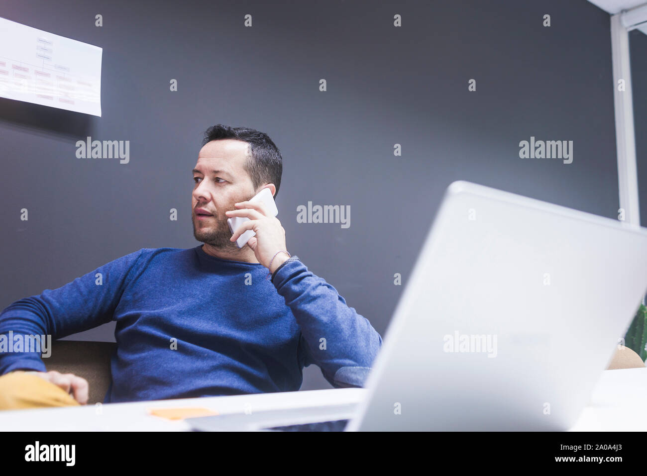 Male executive talking on mobile phone while using laptop at desk Stock Photo