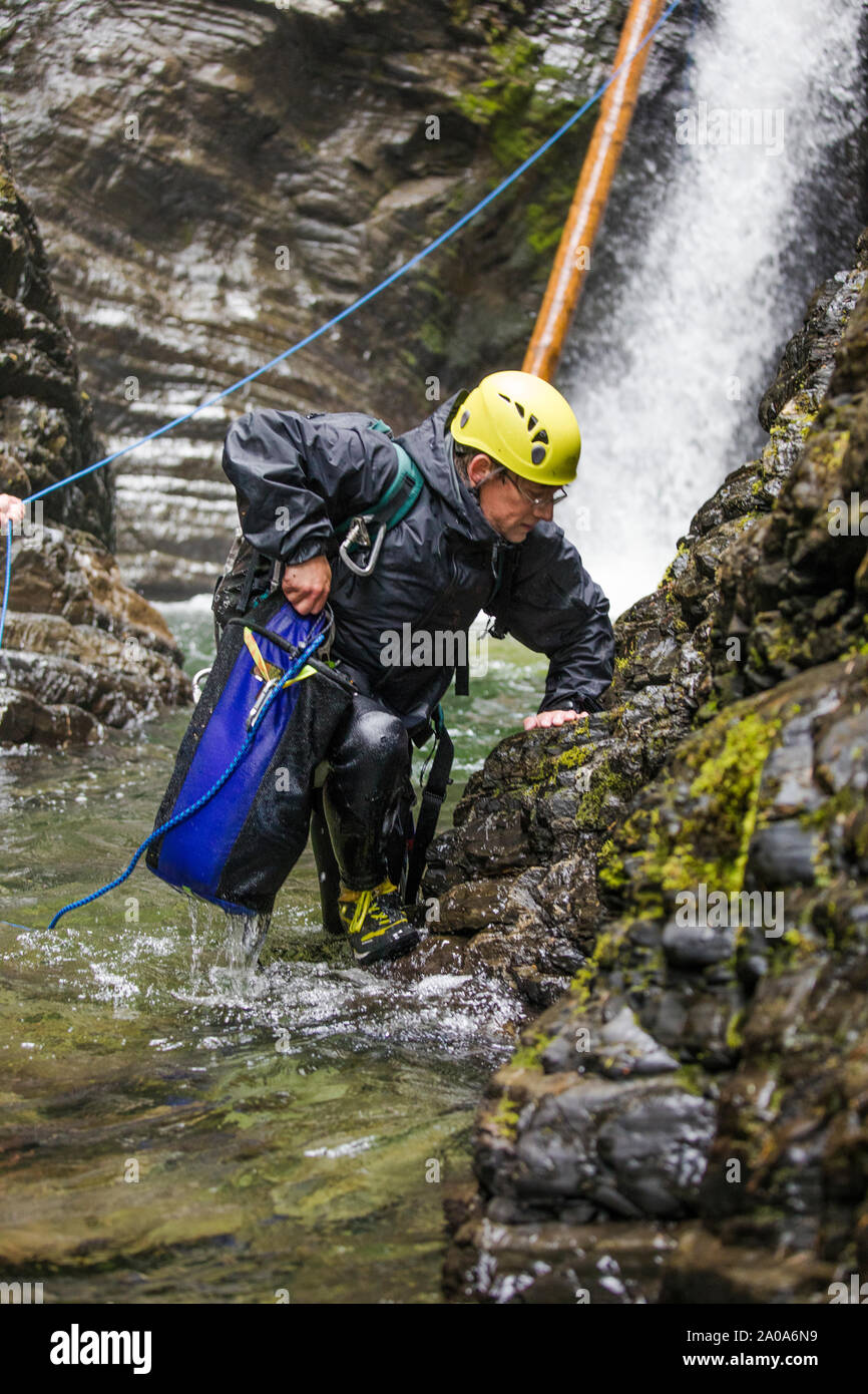 Adventurous man steps out of river after rappelling a waterfall. Stock Photo