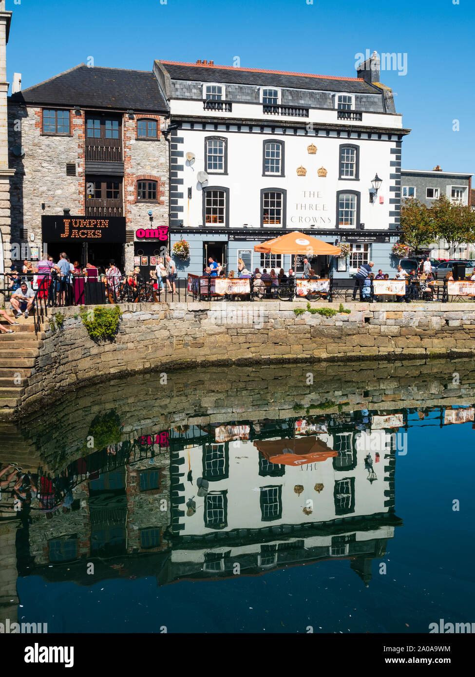 Diners at tables outside the Three Crowns pub reflected in the water of Sutton Harbour, Plymouth Stock Photo