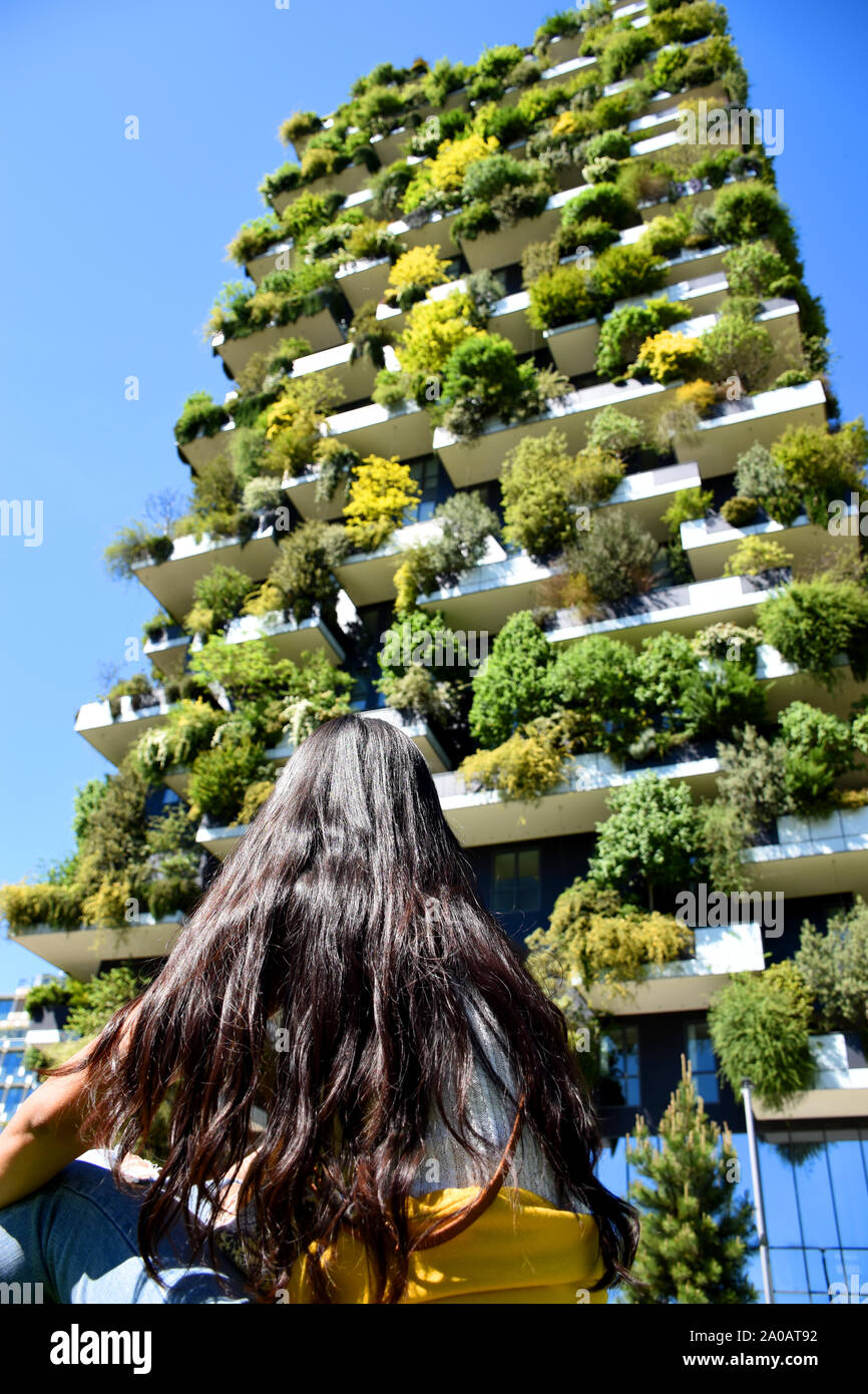 Beautiful thai tanned brunette is sitting in front of the Bosco Verticale (Vertical Forest) residential towers and looking up for the planted 900 tree Stock Photo