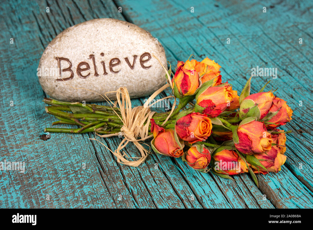 believe text on rock with orange rose bouquet on rustic turquoise painted wood Stock Photo