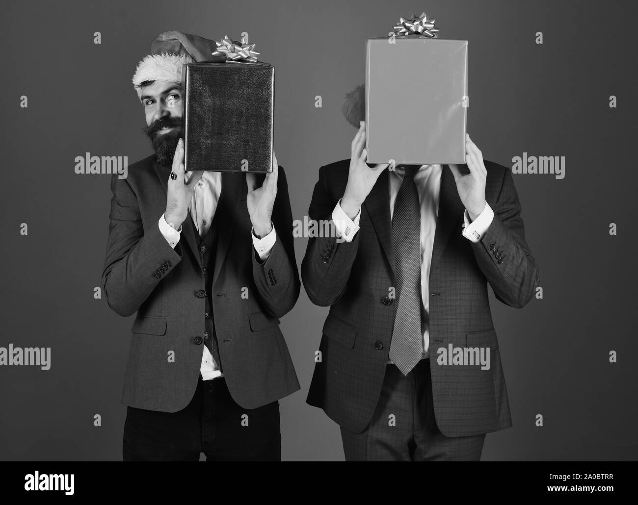 Businessmen Hide Faces Behind Red And Blue Present Boxes Men In Smart Suits And Santa Hats On Blue Background Manager With Beard And Smile Holds Christmas Gift New Year Sales Business Concept