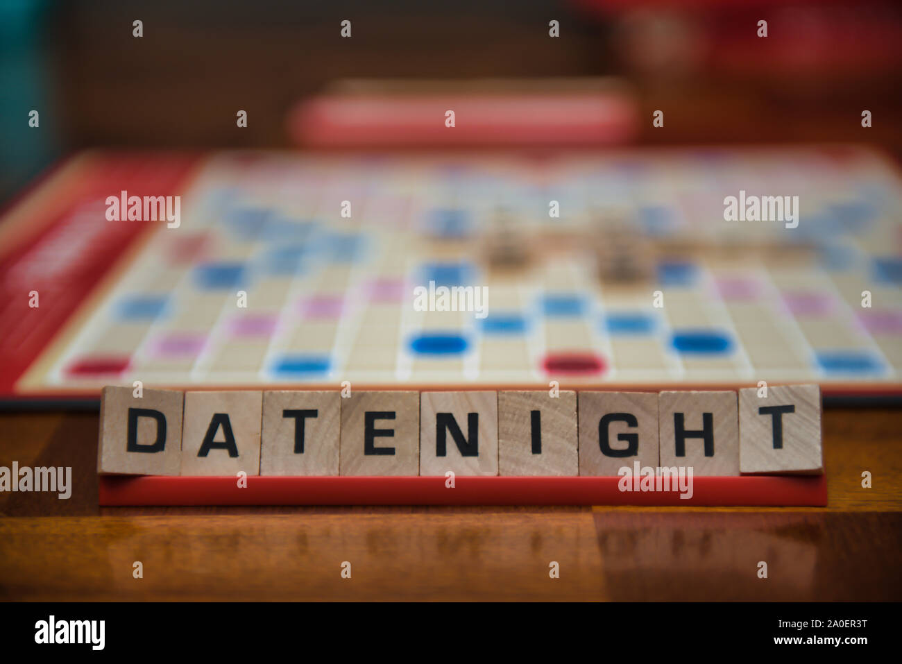 Letter tiles spelling out the words date night on stand in the foreground with out of focus game board in the background. Stock Photo