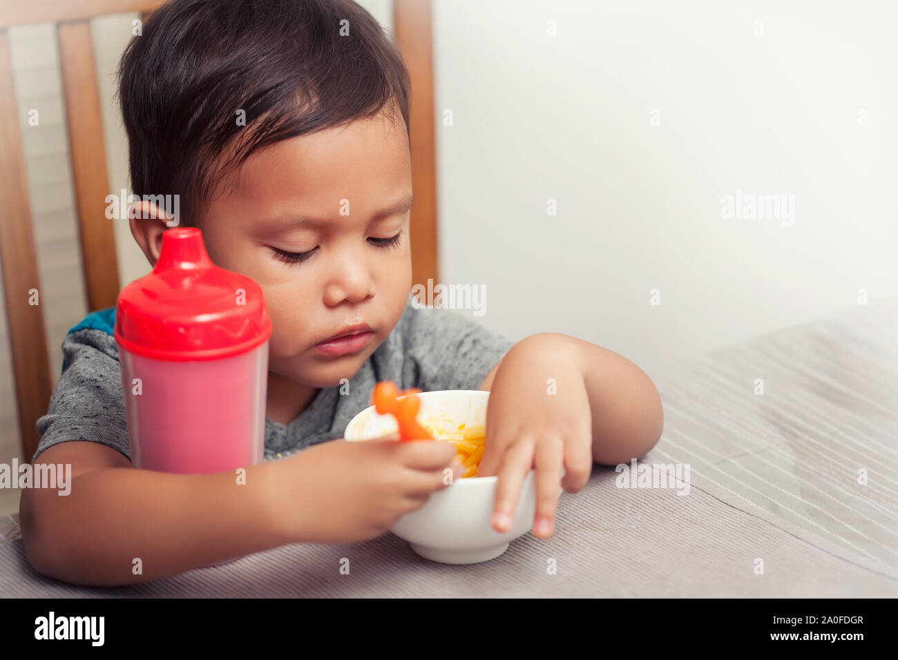 A toddler sitting at the dinner table without a high chair and playing with his food while