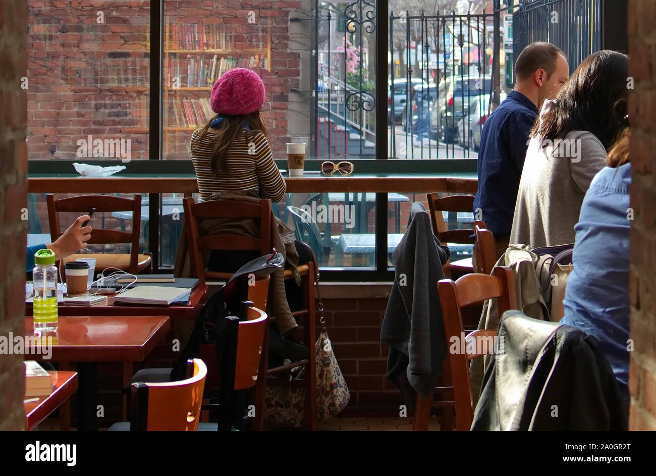 New Haven, CT USA. Mar 2016. Young woman wearing a beret sitting on a cafe high table busy on her phone like most of the customers around her. Stock Photo