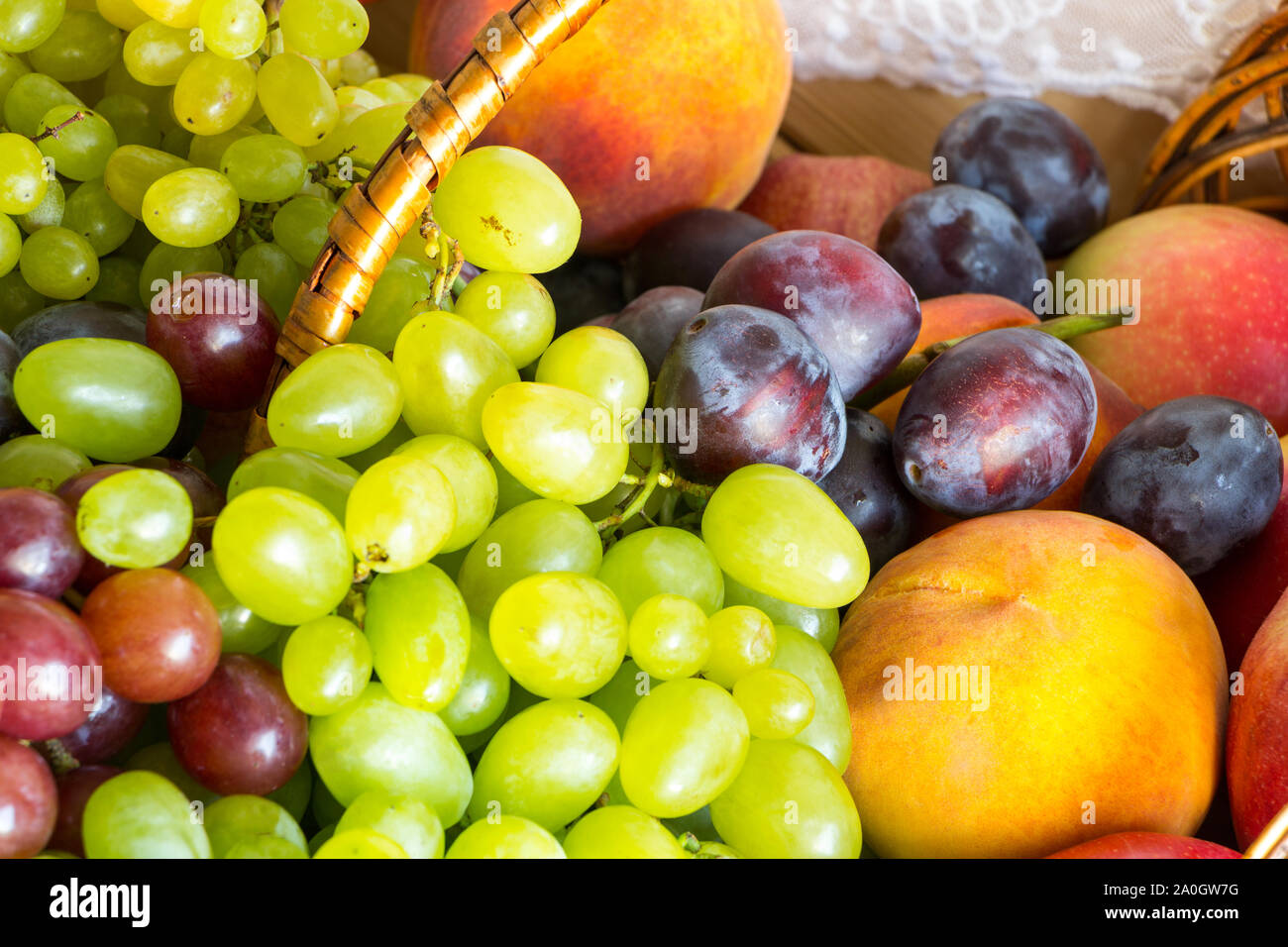 Close up heap of fresh fruits from new harvest poured out from wicker basket on wooden table. Stock Photo