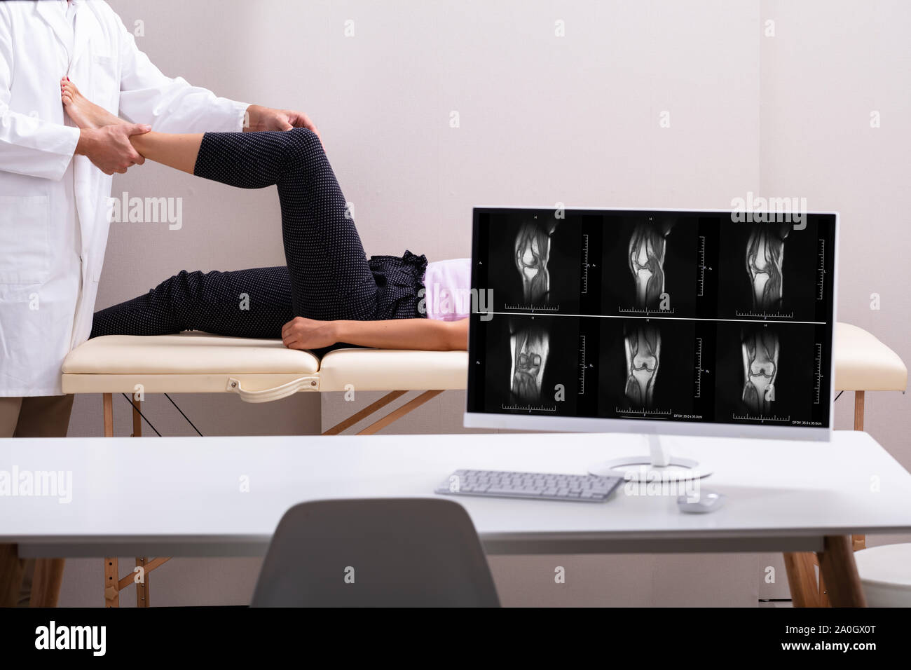 Computer Desk In Front Of Physiotherapist Giving Knee Therapy To Woman Lying In Clinic Stock Photo