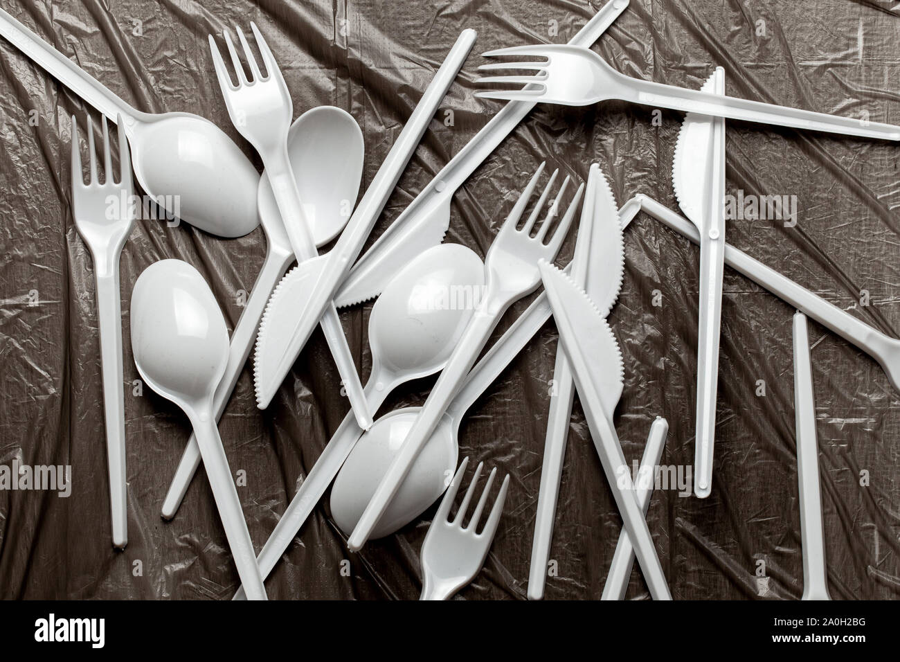 Plastic cutlery, forks, spoons and knives. Pollution of the environment with plastic and microplastics. Black plastic background. Stock Photo