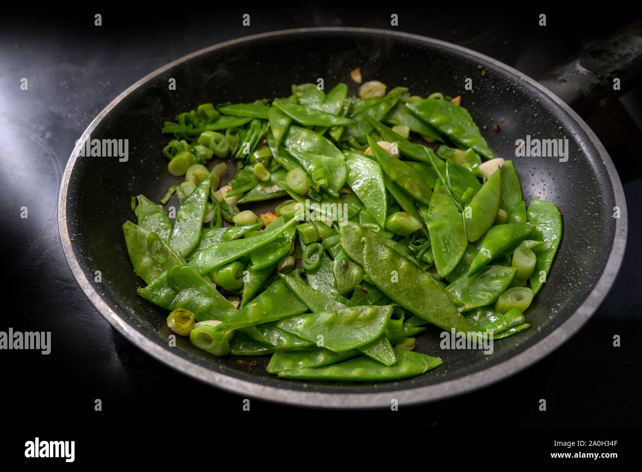 sugar peas and spring onions with garlic are briefly roasted in a pan, cooking healthy
