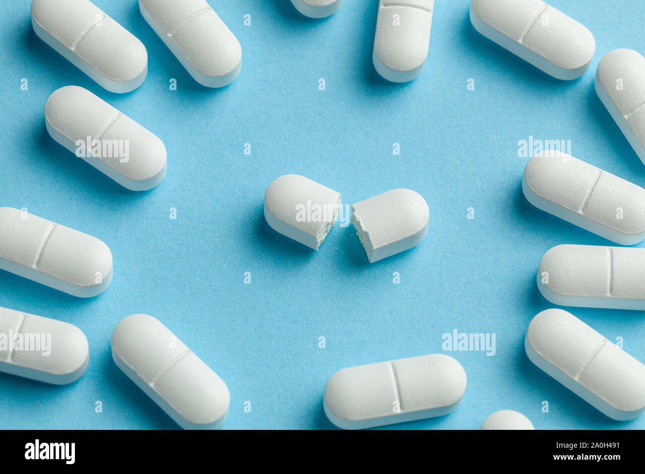 White pills on blue background. One tablet is broken in half, reducing the dose of the medicine