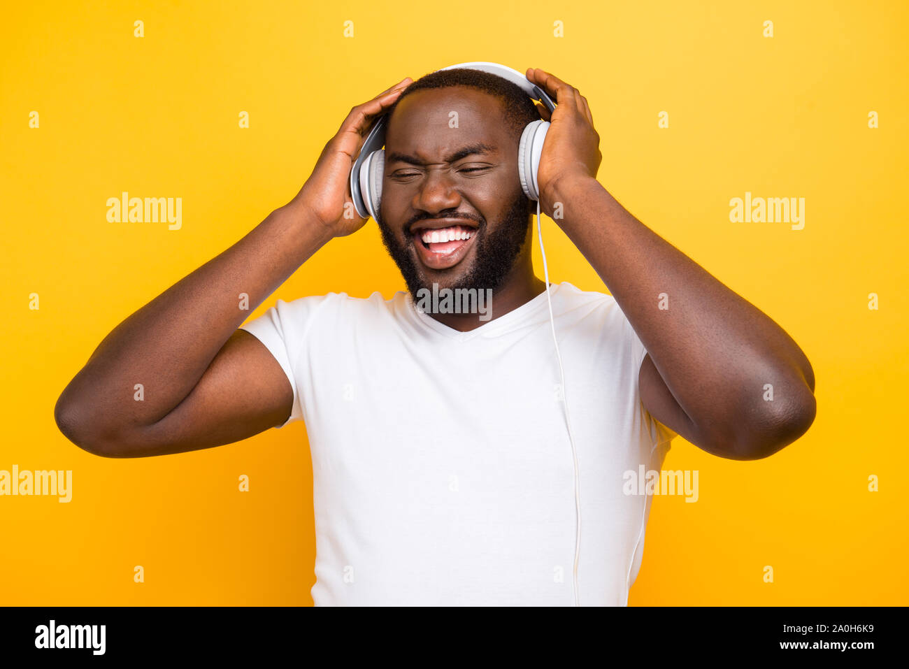 Portrait of handsome shocked mulatto man, holding ear phones with palms, isolated over bright vivid yellow background Stock Photo