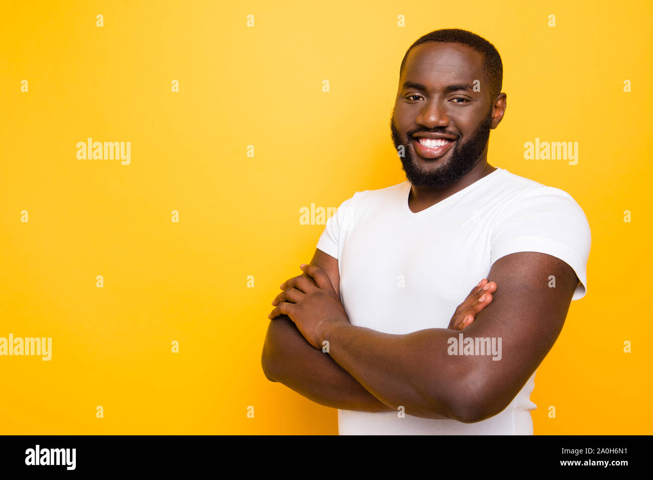 Portrait of handsome content cheerful virile strong mulatto man, crossed arms, isolated over bright vivid yellow background Stock Photo