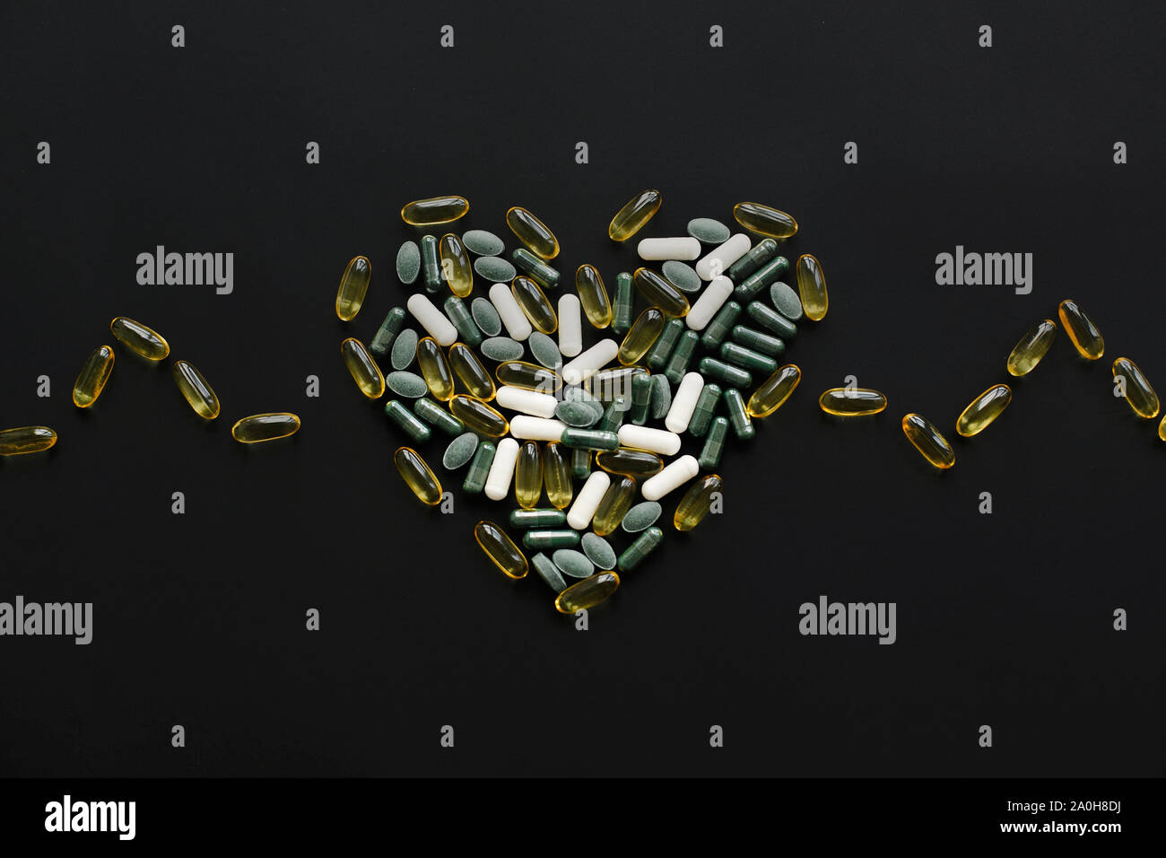 Health support concept. Omega 3, spirulina, chlorophyll, magnesium capsules in heart shape on black dark background. Dietary supplements. Heart made o Stock Photo