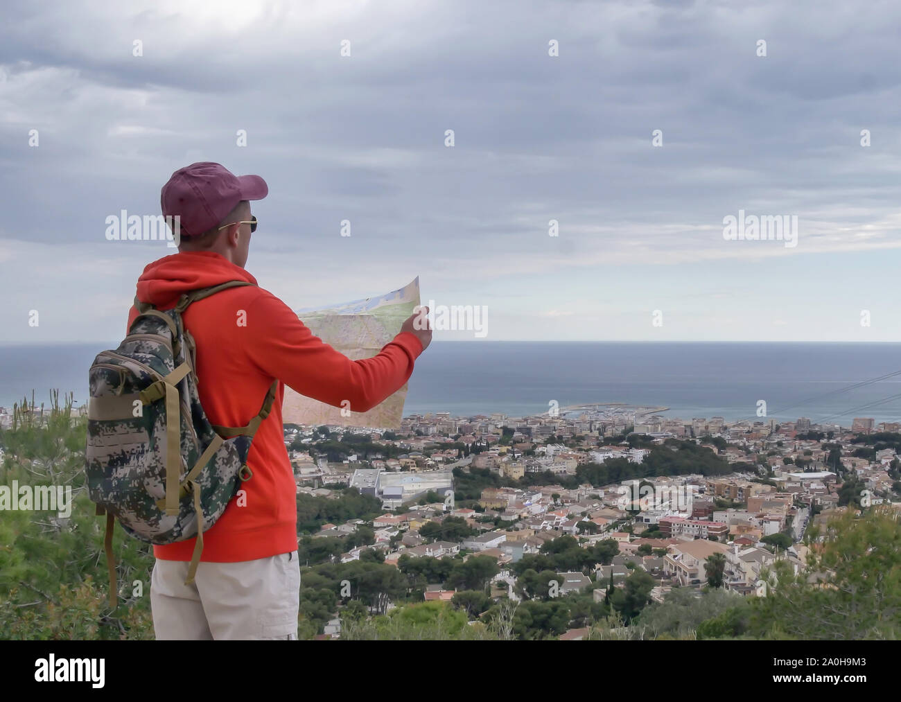 Traveler guy with a map examines the area, a beautiful city by the sea, against a cloudy sky Stock Photo