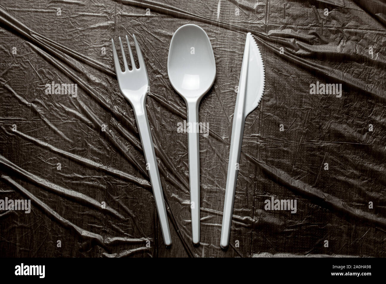 Plastic cutlery, forks, spoons and knives. Pollution of the environment with plastic and microplastics. Black plastic background. Stock Photo