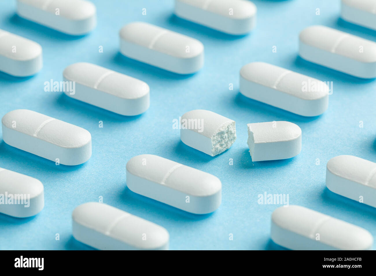 White pills on blue background. One tablet is broken in half, reducing the dose of the medicine. Stock Photo