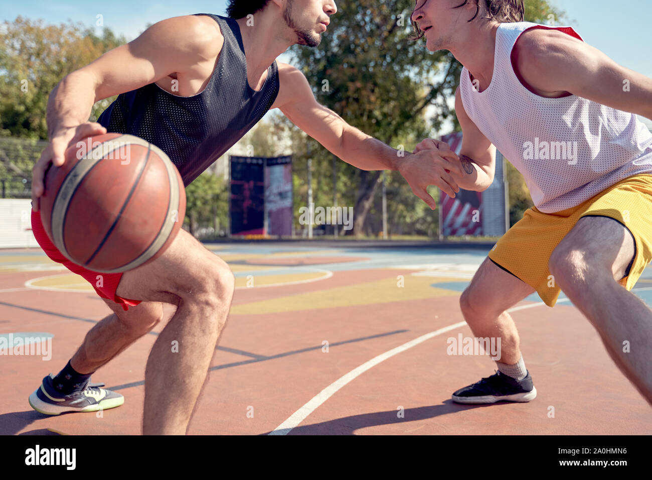 Image of sporty men playing basketball on playground on summer day against background of green trees Stock Photo