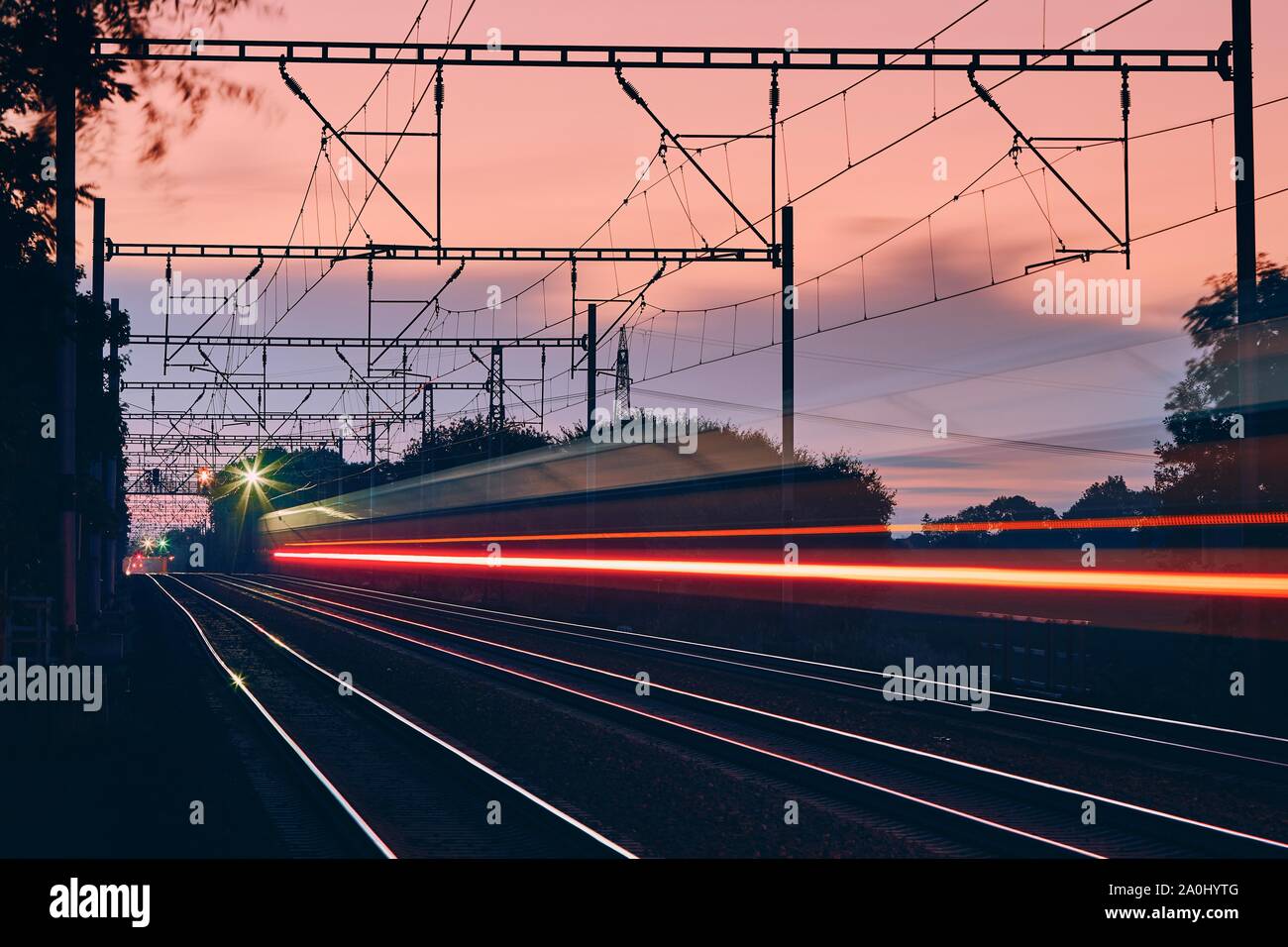 Railway at dawn. Light trails of passenger train on modern railroad track. Stock Photo