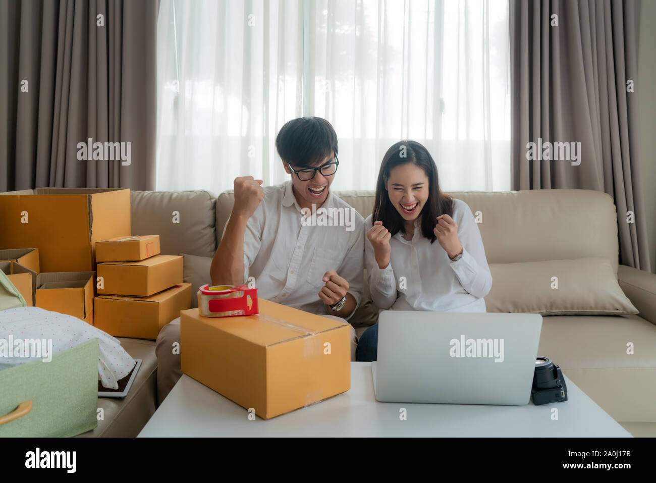 Asian man and woman are selling their online via on the computer in house and very satisfied when there are many of her orders. Small business startup Stock Photo