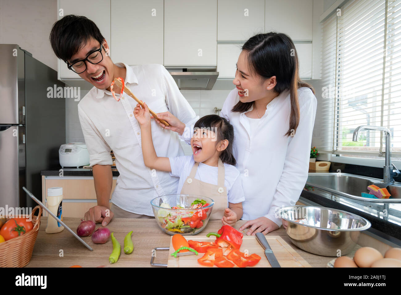 Asian daughters feeding salad to her father and her mother stand by when a family cooking in the kitchen at home. Family life love relationship, or ho Stock Photo