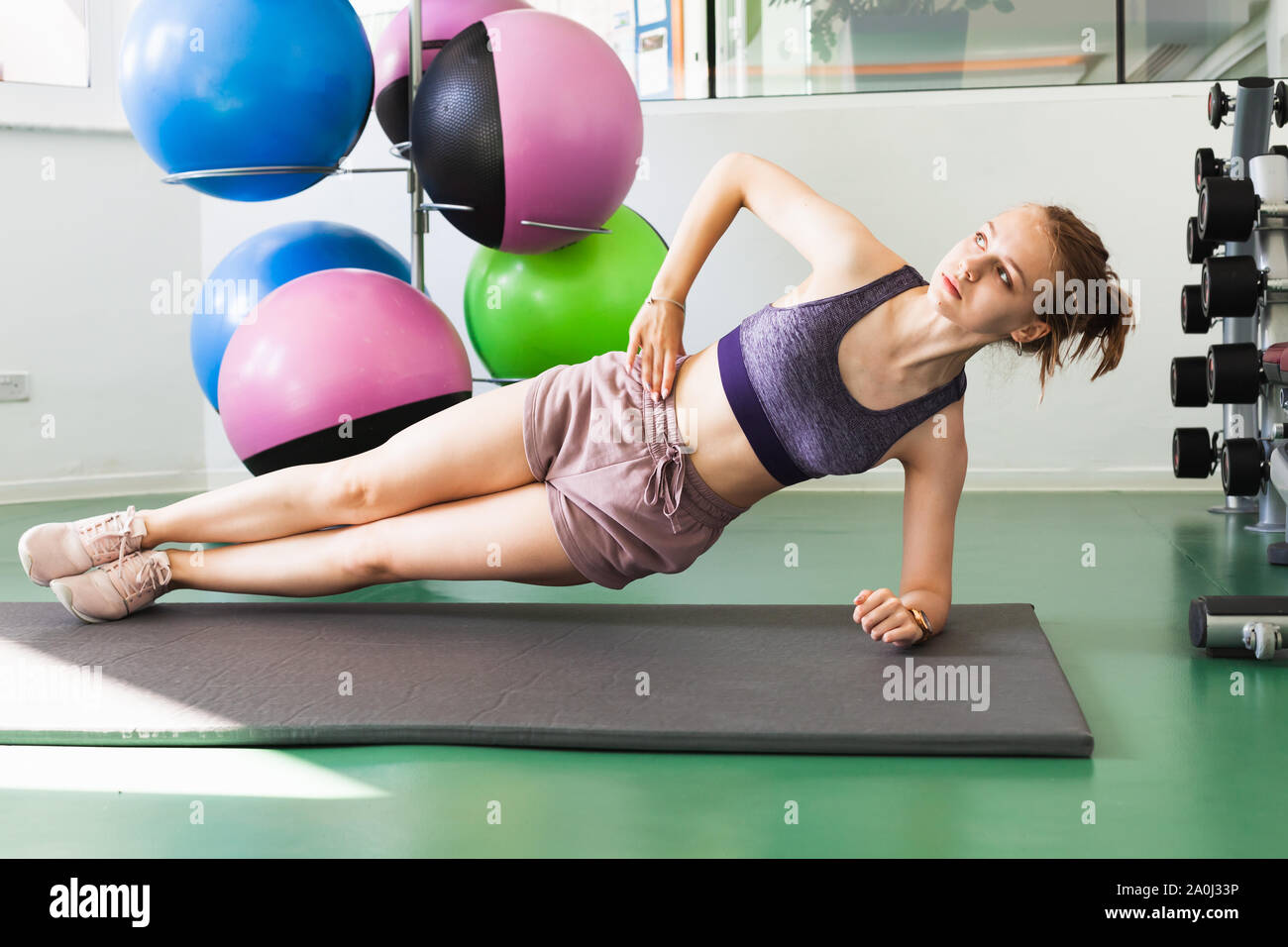 Young blond Caucasian sporty girl does a side plank exercise in a gym Stock Photo